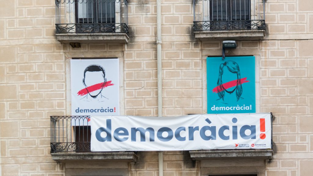 Banner saying "democracy" and pictures of a man and a women with bars over the mouth