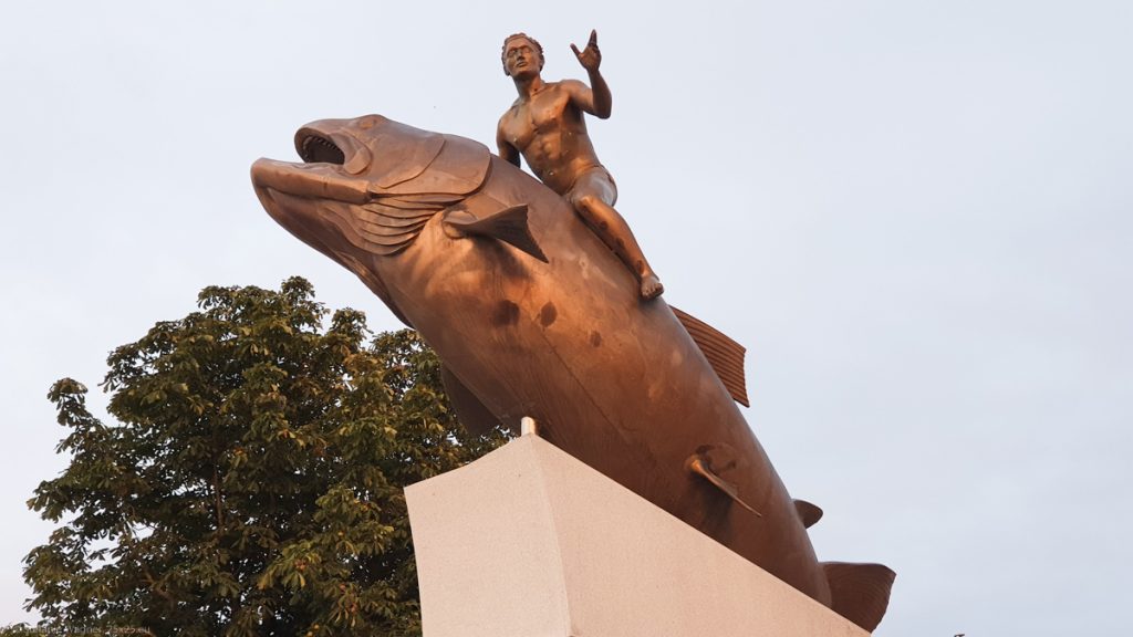 A bronze statue of a fish which seems to jump up and a man riding the fish