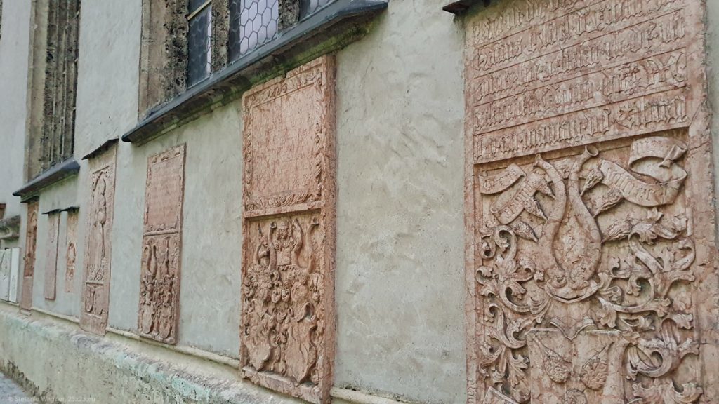 Wall of the church covered with multiple old epitaphs, some of them showing texts at the top and ornaments at the bottom