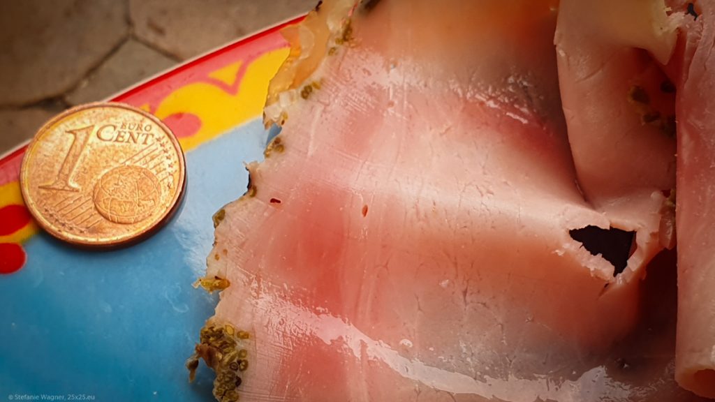 A piece of ham with a hole around the size of 5mm with a Cent coin next to it for comparison