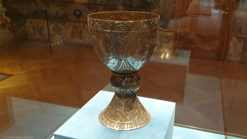 A golden chalice with pictures and text on it.