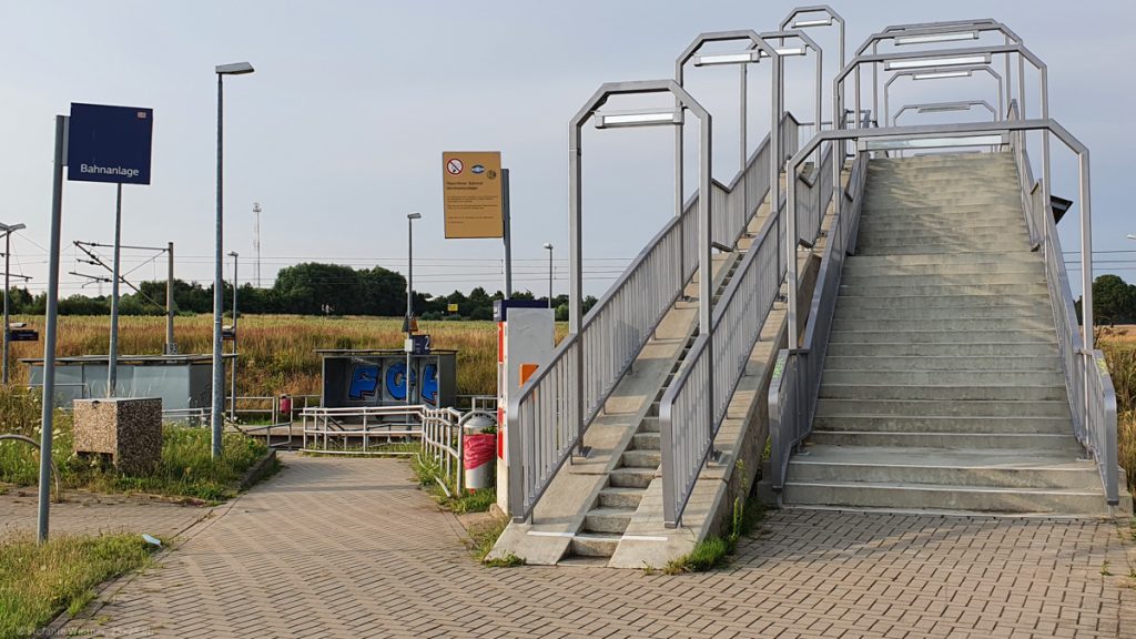 Big concrete stairs with a bridge across rails, small stops in the background