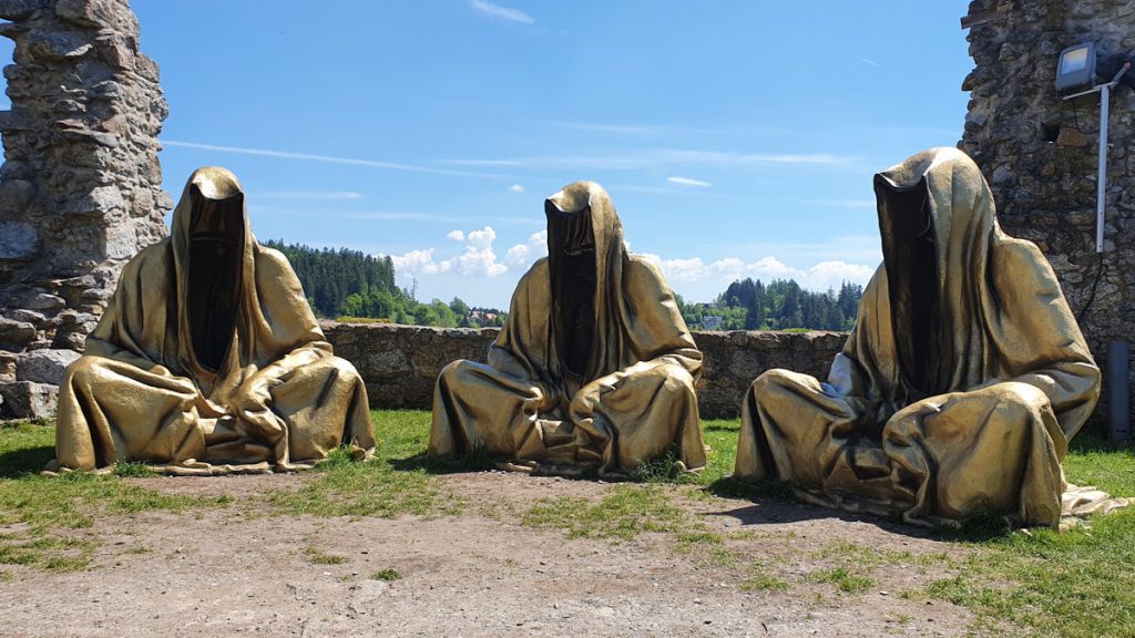 3 huge golden figures sitting like meditating monks, they don't have faces