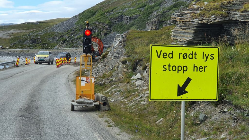 Red traffic light at a construction site with a yellow sign ("Ved rodt lys stopp her")
