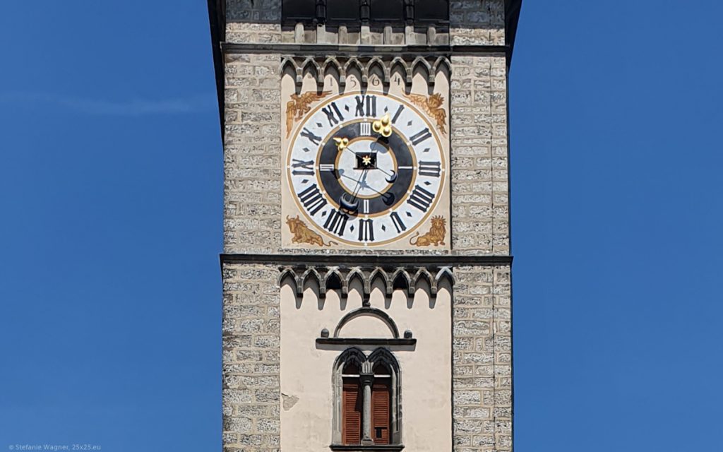 Tower with a big clock, two hands, one longer one with a big golden ending pointing towards just before 1, the shorter one with a small golden ending pointing towards just after 10.