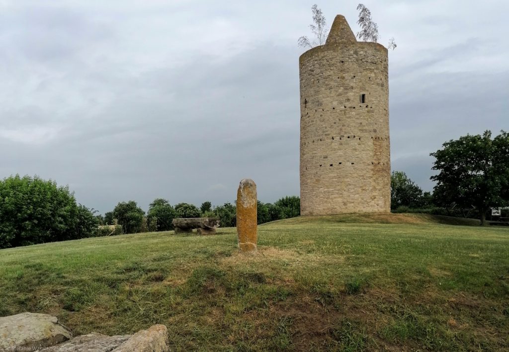 High, round stone tower in the background, stele in the foreground, lawn around
