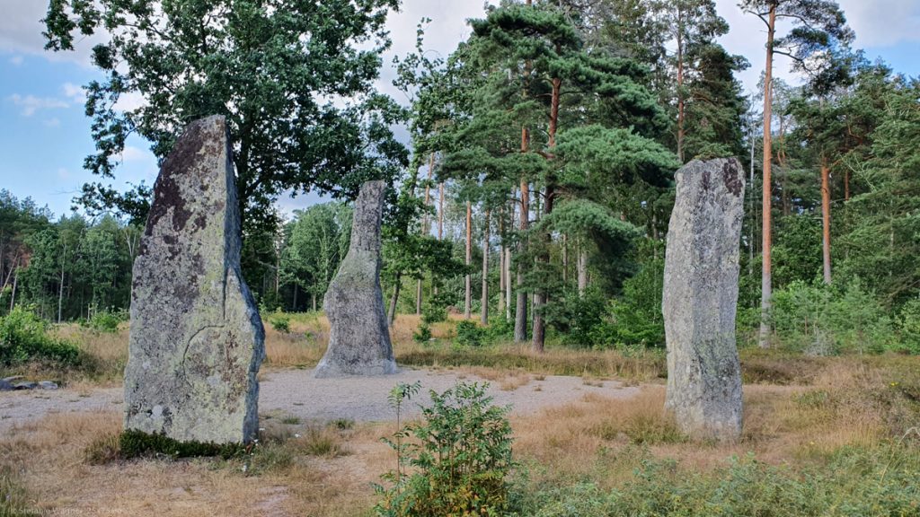 3 gray tall, slim stones set up in a triangle, trees in the background