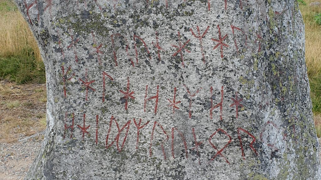 Closeup of the stone, uneven surface, 3 lines of red rune letters