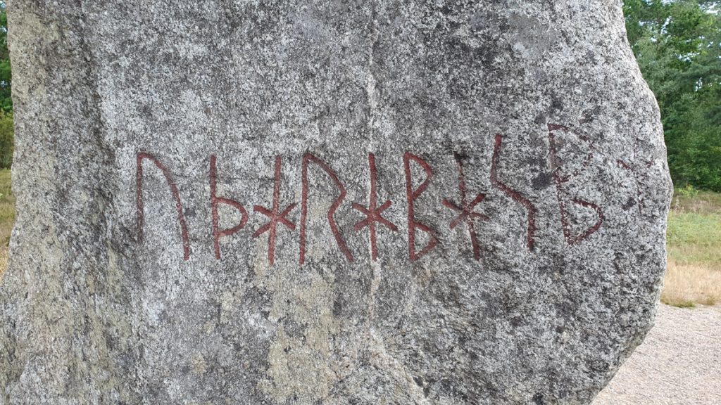 Closeup of the stone, uneven surface, 1 line of red rune letters, more visible that they are engraved
