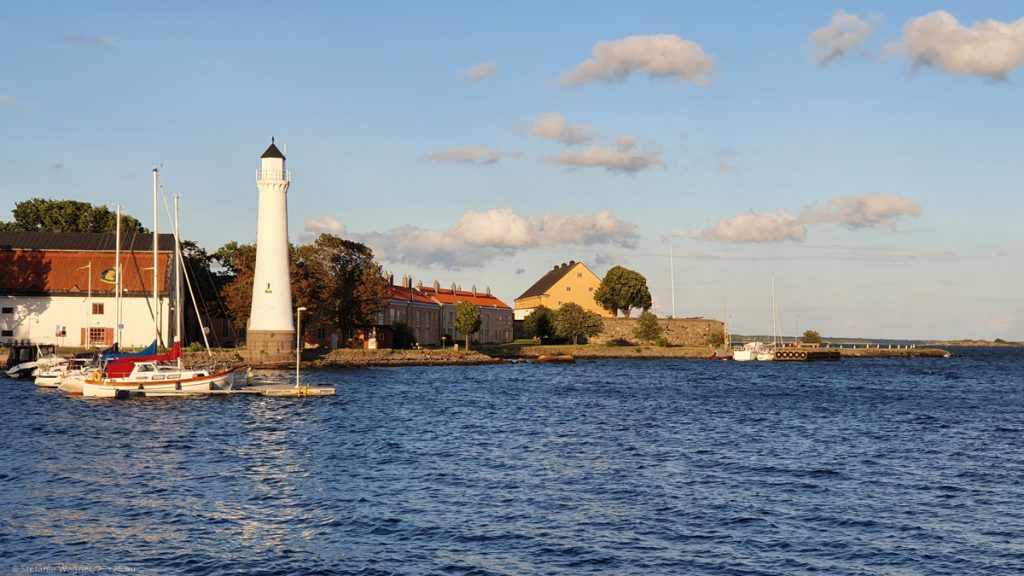 Sea in the lower half, small white lighthouse, some buildings on an island