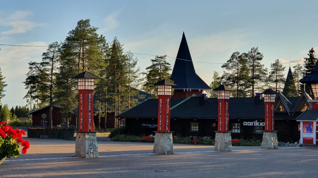 Main square of Santa Claus Village, 4 red columns saying Arctic Circle on stone platforms, a white line between them
