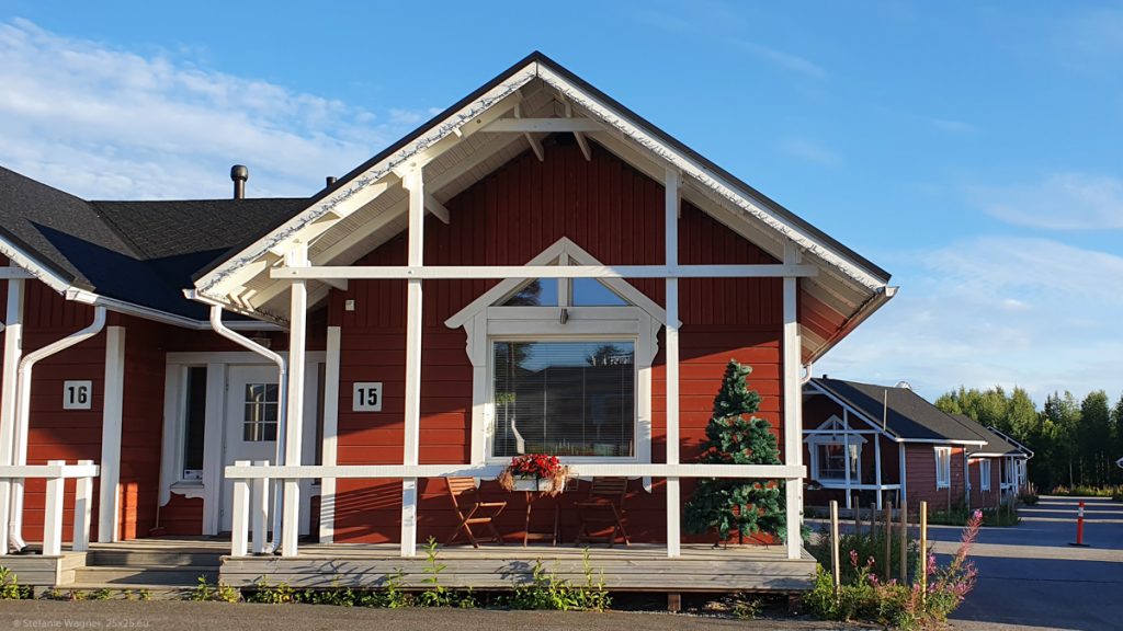 Red wooden house with white frames, small porch with an artificial Christmas Tree