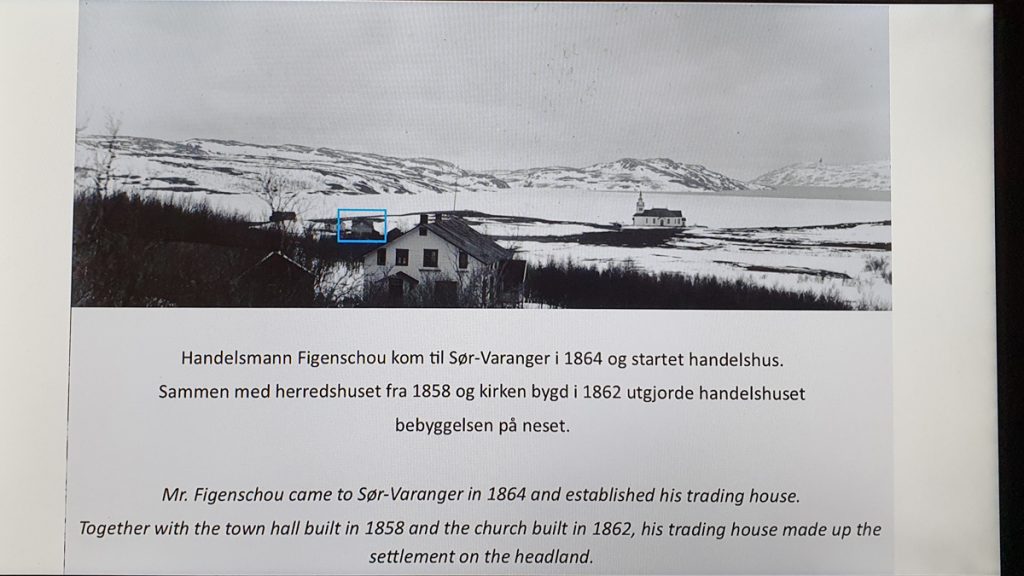 Old picture from Kirkenes showing a church, a small house and a bigger house, water and hills in the background. Text talking about a house being built in 1858 and the church in 1964