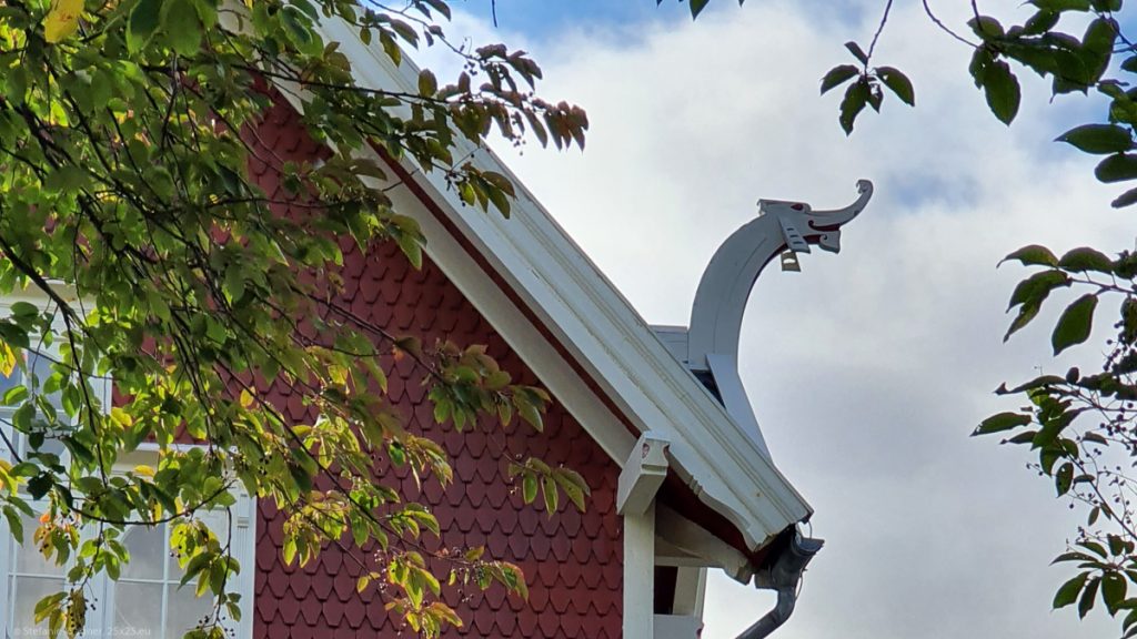 White wooden element on the roof, like a dragon with a long neck and a long nose, looking like it is smiling