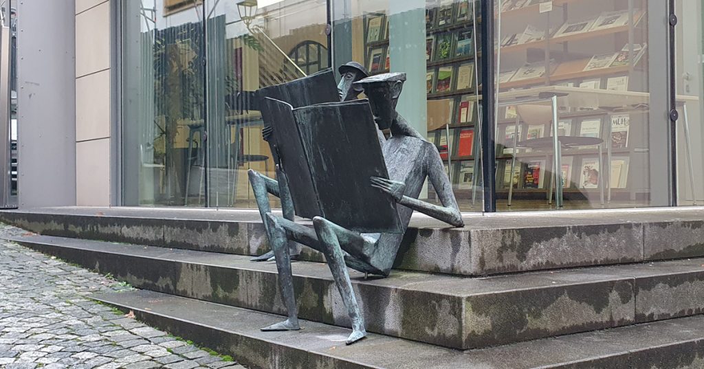 Two metal men with newspapers sitting on the stairs that lead to the library