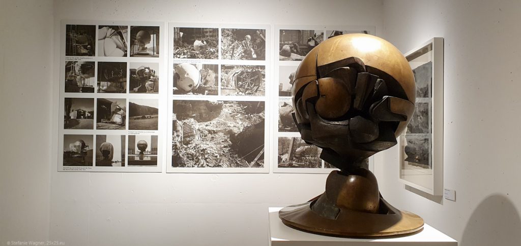 In the background pcitures of the creation and damage of the Sphere, in the foreground a small model of the sculpture.
